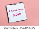 Text words I love you mom on sheet of paper. Happy mothers day concept. Pastel pink background.