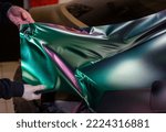 The process of wrapping a car with chameleon-colored vinyl film. A car wrapping specialist covers the car body with vinyl sheet or film. Selective focus.