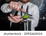 Small photo of Hands of a professional bartender squeeze lime juice with an iron tool with a juicer into a metal shaker, close-up.