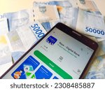 Small photo of Yogyakarta, Indonesia - May 26, 2023. Raya app in Google Play Store, displayed on a smartphone with Indonesian rupiah background. Raya is a digital banking app from PT Bank Raya Indonesia.