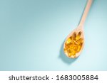 Wooden spoon of Omega-3 capsules on blue background with copyspace. Healthcare, wellbeing and supplements.