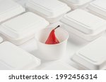 Red wine poached pear in a paper cup among white takeaway boxes. Minimalistic photo of gourmet dessert for delivery.