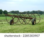 Small photo of old rusty windrow hay making equipment in a farm field