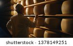 Cheesemaker is controlling the seasoning lots of wheels of parmesan cheese are maturing by ancient Italian tradition for many months on shelves of a storehouse in a dairy factory.