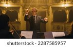 Small photo of Cinematic Close Up of Conductor Directing Symphony Orchestra with Performers Playing on Stage During Music Concert. Professional Conductor Leading Musicians Passionately in Classic Theater