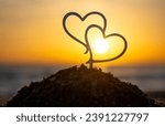 Small photo of Two black outlines of heart at dawn and sunset on sky on seashore. Stick contours in shape of heart in sand on backdrop of setting and rising sun on seashore. Concept Love infatuation Valentine's Day