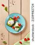 Small photo of Avocado toast with poached eggs and vegetables in rustic style. Healthy breakfast - toasts with avocado, tomatoes and eggs on wooden background. Colourful morning composition with trendy food