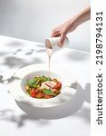Small photo of Summer salad with octopus and pouring sauce. Female hand with gravy boat. Hand pouring sauce on seafood salad. Action food menu. Trendy concept menu
