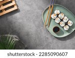 Small photo of Modern japanese food concept. Maki sushi on ceramic plate with soy sauce and chopsticks on stone background. Aesthetic composition with sushi roll on dark concrete backdrop. Yin yang maki roll