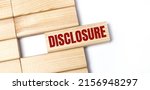 Small photo of On a light background, wooden blocks with the text DISCLOSURE. Close-up top view.