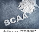 Small photo of BCAA branched chain amino acid text made of powder on grey background with scoop and dumbbell used by bodybuilders before workout as a pre-workout supplementation