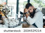 Small photo of Worried Barista Using Digital Tablet in a Cafe. Distraught sad waiter with a beard leaning on the bar counter and looking away while waiting for order in the restaurant or a coffee shop.