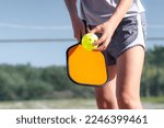 Small photo of Pickleball paddle and yellow ball close up, woman playing pickleball game, hitting pickleball yellow ball with paddle, outdoor sport leisure activity.