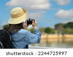 Rear view of woman traveller with backpack taking photo with digital camera while standing on a bridge over a canal