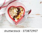 Muesli in heart shaped bowl, white wood background, top view