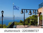 Greek flag on a pole with the Bells  of Saint Patapios monastery in Loutraki, Corinthia, Peloponnese, Greece.   Sunny day with blue sky.