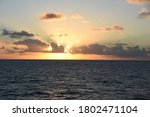 Sunset in Atlantic ocean during calm weather with the sun behind the heap clouds. Sunrays have orange colour.  Picture was taken from the navigational bridge of the cargo container vessel.