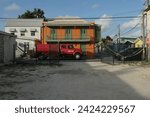 Small photo of Bridgetown, Barbados 02 02 2024: Typical house in bright colours and colonial style on the Caribbean island of Barbados in Bridgetown. In front is passing the old red cable repair truck.