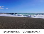Turquoise waves of the Mediterranean sea on a black volcanic beach.  Coast near Taormina, Sicily, Italy