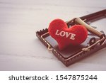 Small photo of Red heart in a rat trap on white wooden background. Online internet romance scam, swindler or valentine day in darkside concept. Love is bait or victim.