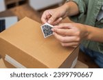 Small photo of Close-up: A woman's hands affix a QR code sticker to a package, epitomizing the e-commerce delivery and online shopping experience.
