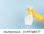 Hand in yellow protective rubber glove holding spray bottle with detergent against blue background with copy space. Cleaning product for different kitchen or bathroom surfaces. Bleach. Mockup
