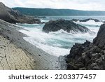 shore in natural lava causeway, sea surf among coastal rocks overlooking the distant shore