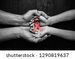 AID red ribbon in hands on a black wooden background, World Cancer Day, symbol of the fight against HIV, AIDS and cancer. concept of helping those in need. black and white.