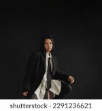 Small photo of A young African American woman sits on a chair in a business suit on a black background. A pretentious young black woman.