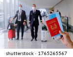 Travel concept. Hand holding Singapore passport, with boarding pass and face mask. Pilots walking in the background with luggage. Reopening; coronavirus covid-19; travel restrictions.