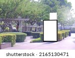 Small photo of Vertical blank advertising poster billboard banner mockup; lush plants and tress in background; digital light box display screen for OOH out of home media