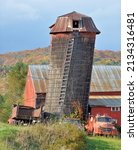 Small photo of Amusing scene in rural Vermont with leaning hay silo, weathered red barn, and vintage fire engine. Heavy wire wrapped around silo and attached to old dump truck to keep tipsy silo from falling over.
