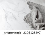 Wrinkled light grey pure linen towel on empty white marble board. Light marble background with copy space.
