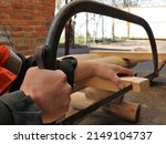 Small photo of sawing off the edge of a bar in the structure of a wooden structure with an arc saw in a rural yard, a hand saw in the process of woodworking in a village, hacksaw work in a village yard