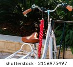 Retro city bike with red closed umbrella hanging on synthetic leather handlebar grip , white stylish bicycle, green bushes on background