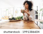 Young african american woman drinking green juice with reusable bamboo straw in loft apartment. Home concept. Healthy lifestyle concept. Copy space