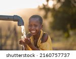 Small photo of Mali,Kenya - Agust 23 2021:happy boy drinking water from water pump, water well in village in africa.