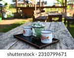 Small photo of Empty enamel mugs and enamel teapot on wooden table. Selective Focus.