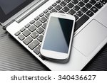 Blank White Business Smartphone With Reflection Lying On A Notebook Keyboard, All Above A Carbon Layer