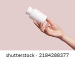 Small photo of Female hand holding blank white squeeze bottle plastic tube on pink background. Packaging for pills, capsules or supplements. Mockup. High quality photo