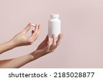 Small photo of Woman holding pill and blank white plastic tube on pink background. Packaging for pill, capsule or supplement. Medic product branding mockup. High quality photo