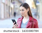 Perplexed woman checking smart phone news standing in the street