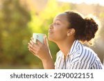 Profile of a relaxed black woman drinking coffee and smelling aroma in a park
