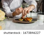 professional caucasian chef-cook decorate dish in the kitchen. man in white apron makes the finishing touch on the dish. culinary, food, restaurant, gourmet concept