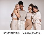 beauty portrait of diverse women, caucasian, asian and african american ladies with different skintone posing at camera, hugging each other, dressed casually in beige tone clothes. isolated