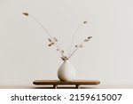A bunch of  dried bunnytail flower in a white ceramic vase on a brown wooden board. Simple and minimal home decoration. White wall, copy space. 