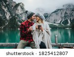 Portrait of a romantic couple of adults visiting an alpine lake at Braies Italy at winter. Tourist in love drinking hot coffee at mountains. Couple, wanderlust and travel concept.