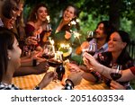 Small photo of Happy family celebrating with fireworks at barbecue backyard party - Young people having fun with fire sparklers at night time - Friends drinking red wine at farmhouse restaurant - Youth concept