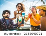 Happy young people cheering cocktail glasses together at beach party - Multi-ethnic friends enjoying happy hour sitting at bar table - Youth lifestyle and summertime vacations concept - Focus on eyes