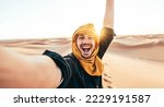 Small photo of Happy male tourist taking selfie on sand dunes in the Africa desert, Sahara National Park - Influencer travel blogger enjoying trip while takes self portrait - Summer vacation and weekend activities